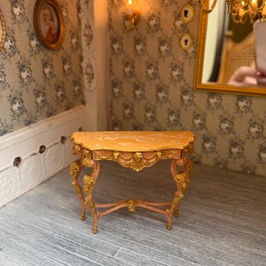 May include: A miniature pink and gold console table with ornate details and a marble top.