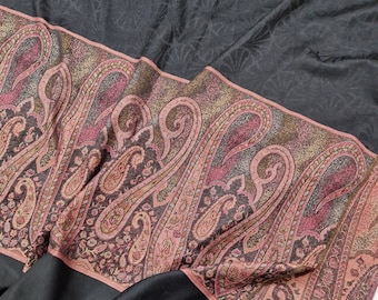 May include: A black shawl with a paisley patterned border in shades of pink, brown, and gold. The shawl has a fringe on the bottom edge.