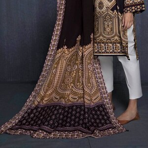Puede incluir: Un vestido estampado en marrón y dorado con una chal marrón a juego. El vestido tiene manga larga y cuello redondo. El chal tiene un diseño de cachemira.