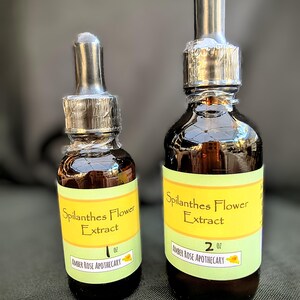 May include: Two amber glass bottles of Spilanthes Flower Extract with dropper tops. The bottles have yellow and green labels with the text "Spilanthes Flower Extract" and "Amber Rose Apothecary". One bottle is 1 oz, the other is 2 oz.
