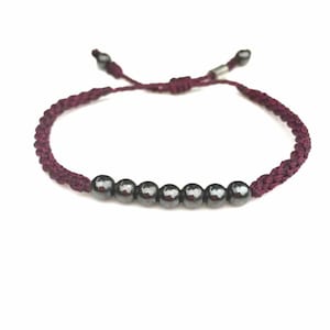 Peut inclure: Un bracelet en cordon tressé bordeaux avec une rangée de six perles argentées.