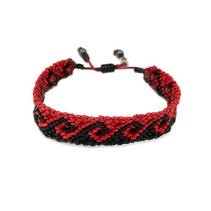 May include: A red and black friendship bracelet with a geometric pattern.