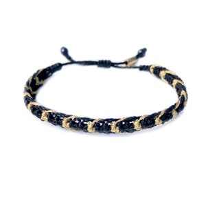 May include: A black and gold braided bracelet with a sliding knot closure.