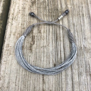 Silver string bracelet for awareness and support, featuring a sleek and minimalist design. This handmade silver awareness jewelry raises awareness for schizophrenia, Parkinson’s, dyslexia, and sciatic pain. Its fully adjustable fit makes it suitable for men, women, and kids. The silver ribbon awareness bracelet is a thoughtful gift to show support for loved ones. Rumi Sumaq jewelry, silver awareness bracelet, disabled children wristband, Parkinson’s awareness wristband.