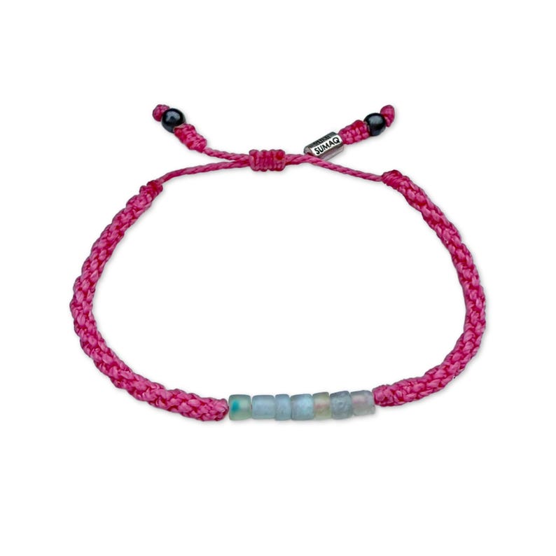 Handmade pink Peruvian Opal bracelet by Rumi Sumaq, intricately hand-knotted by Indigenous Quechua artist Coco in his Martha’s Vineyard studio. The bracelet features seven genuine Peruvian Opal stones, Hematite bead accents, and a silver-toned Rumi Sumaq logo bead. Its soft pink waterproof fiber adds a feminine touch, balancing elegance and everyday wearability. Adjustable and unisex, it’s perfect for birthdays, anniversaries, or meaningful October gifts.