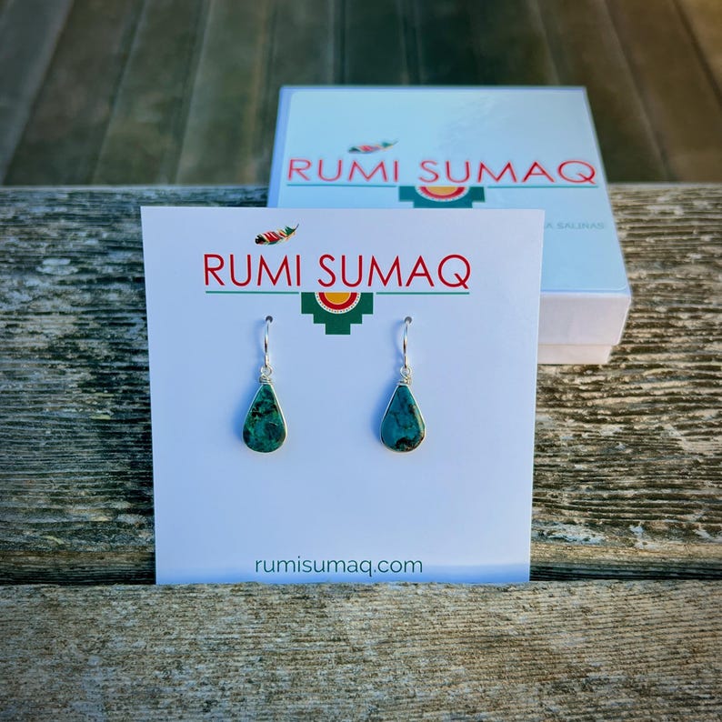 Closeup of Chrysocolla teardrop earrings in a Rumi Sumaq gift box. Chrysocolla teardrop necklace and dangle earrings set handcrafted on Martha’s Vineyard by Rumi Sumaq. The pendant necklace features a wire-wrapped Chrysocolla gemstone on a delicate sterling silver or gold fill chain, available in 16-inch, 18-inch or 20-inch lengths. Matching earrings dangle from French ear wires for a cohesive look. This healing stone jewelry set makes a meaningful gift and arrives in a Rumi Sumaq gift box.