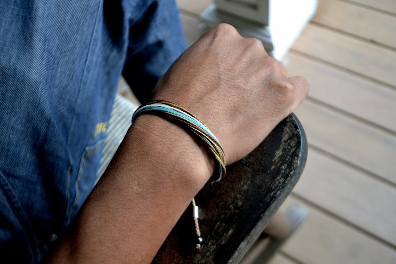 Peut inclure: Un bracelet en cordelette multicolore avec des fils marrons, blancs et bleus. Le bracelet est nou&eacute; et comporte une petite perle noire &agrave; l'extr&eacute;mit&eacute;.