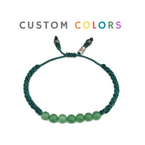 May include: A green braided bracelet with a row of green jade beads. The bracelet has a silver tag with the word "CUSTOM" on it.