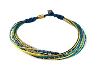 Può includere: Un braccialetto multicolore con fili blu, gialli, bianchi e neri. Il braccialetto è realizzato con cordoncino intrecciato e ha una chiusura dorata.