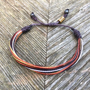 May include: A multi-coloured braided bracelet with a gold charm that says "LOVE IS", and black beads on each end.