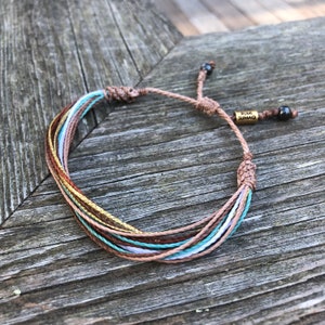 Peut inclure: Bracelet en cordelette multicolore avec un charme dor&eacute; qui dit "RUMI SUMAQ".