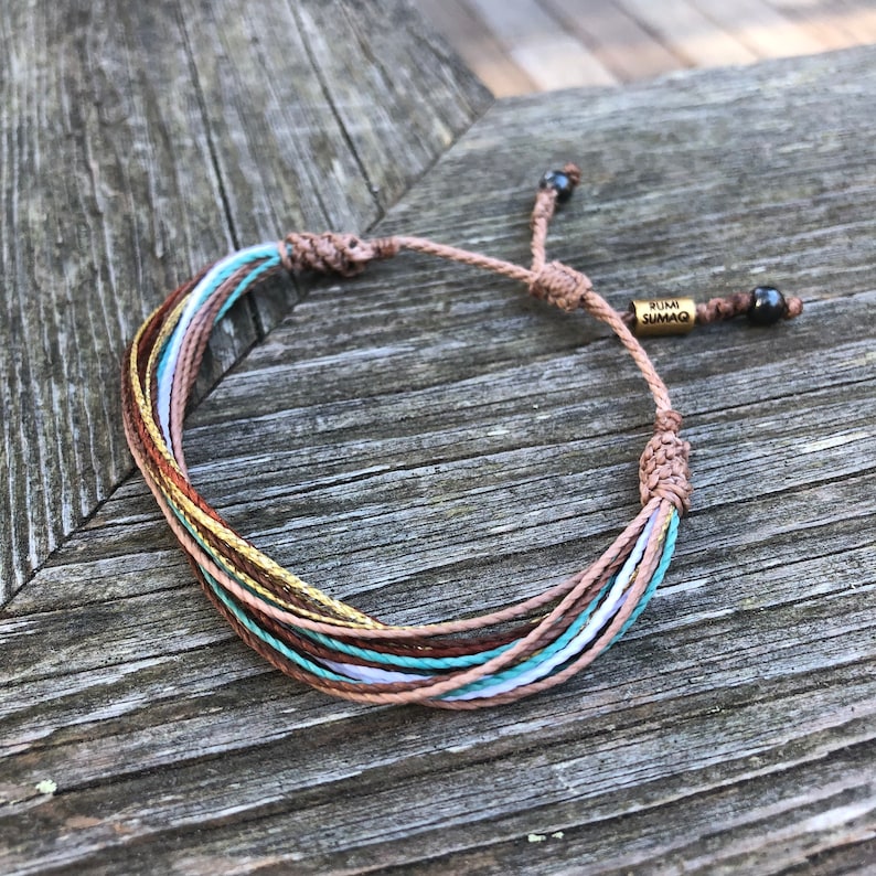 Peut inclure: Bracelet en cordelette multicolore avec un charme dor&eacute; qui dit "RUMI SUMAQ".