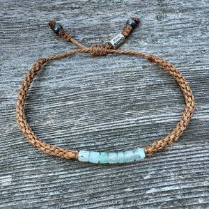 Custom tan rope Peruvian Opal bracelet by Rumi Sumaq featuring seven genuine Peruvian Opal stones, Hematite beads, and a silver tone logo bead. Hand-knotted by Indigenous Quechua artist Coco in the Martha’s Vineyard studio. Adjustable, waterproof, and unisex for men, women, or kids. Ideal October birthstone or 24th wedding anniversary jewelry gift.