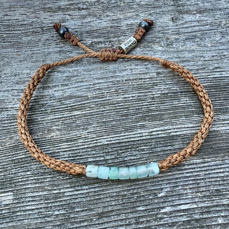 Custom tan rope Peruvian Opal bracelet by Rumi Sumaq featuring seven genuine Peruvian Opal stones, Hematite beads, and a silver tone logo bead. Hand-knotted by Indigenous Quechua artist Coco in the Martha’s Vineyard studio. Adjustable, waterproof, and unisex for men, women, or kids. Ideal October birthstone or 24th wedding anniversary jewelry gift.