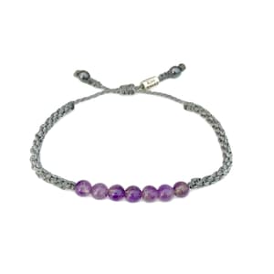 May include: Gray braided bracelet with a row of six purple amethyst beads and a silver tag that reads "RUMI"