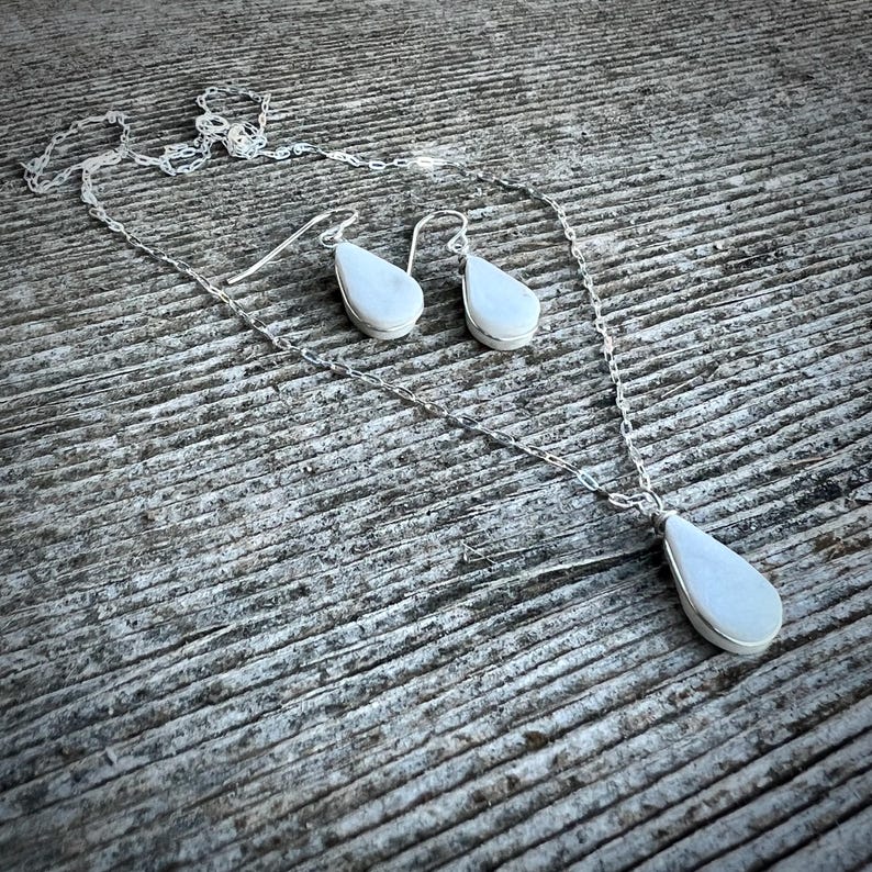 This handmade white jasper necklace and earrings set is a stunning piece of healing crystal jewelry crafted by Quechua designer Coco Paniora Salinas in his Rumi Sumaq art jewelry studio on Marthas Vineyard. The teardrop white jasper pendant necklace and matching earrings are available in silver or 14k gold fill making them an elegant choice for everyday wear or spiritual healing. Known for its calming energy white jasper enhances balance and clarity making this an ideal energy healing gift.