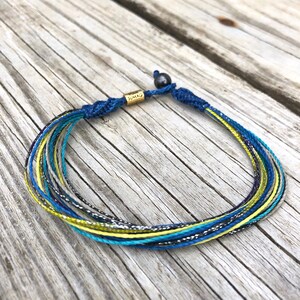 Boho beach anklet for men, women, and children, handcrafted with care on Martha’s Vineyard.  This unique macramé rope anklet in blue, yellow, aqua and purple features a non-adjustable design with a secure Hematite stone toggle closure. This waterproof anklet is perfect for surfers, sailors, and outdoor enthusiasts. Durable and stylish, it’s a must-have for summer and travel. A great gift for surfers and beach enthusiasts.