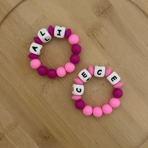 May include: Two pink and purple silicone bracelets with the names "Alice" and "Grace" spelled out in white letters.