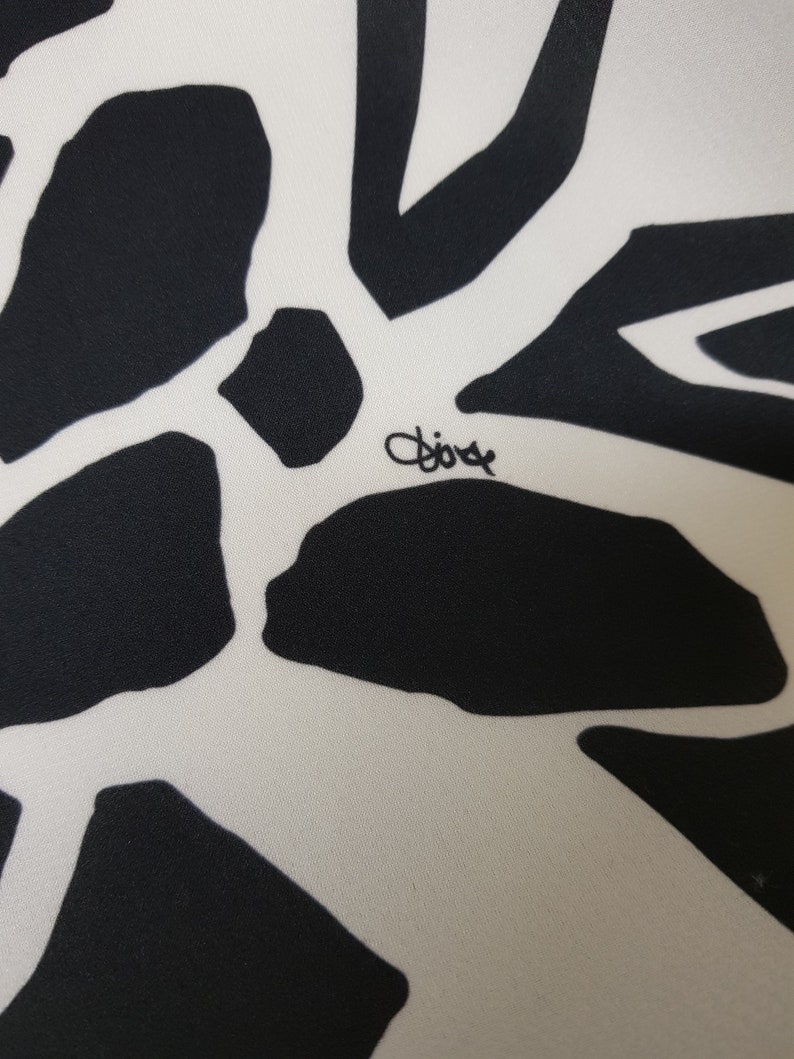 Puede incluir: Primer plano de una tela blanca con un patr&oacute;n abstracto en blanco y negro. La tela tiene la palabra "Dior" escrita en tinta negra.