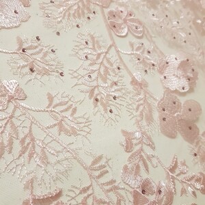 May include: Pink floral lace fabric with delicate embroidery and small, shiny beads.