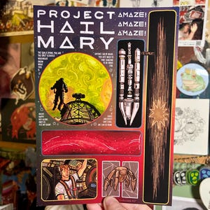 May include: An art print with the words "PROJECT HAIL MARY" and space-themed illustrations. It depicts a figure on a planet, a spaceship, and a spider-like creature. The print also includes various quotes and star-like designs.
