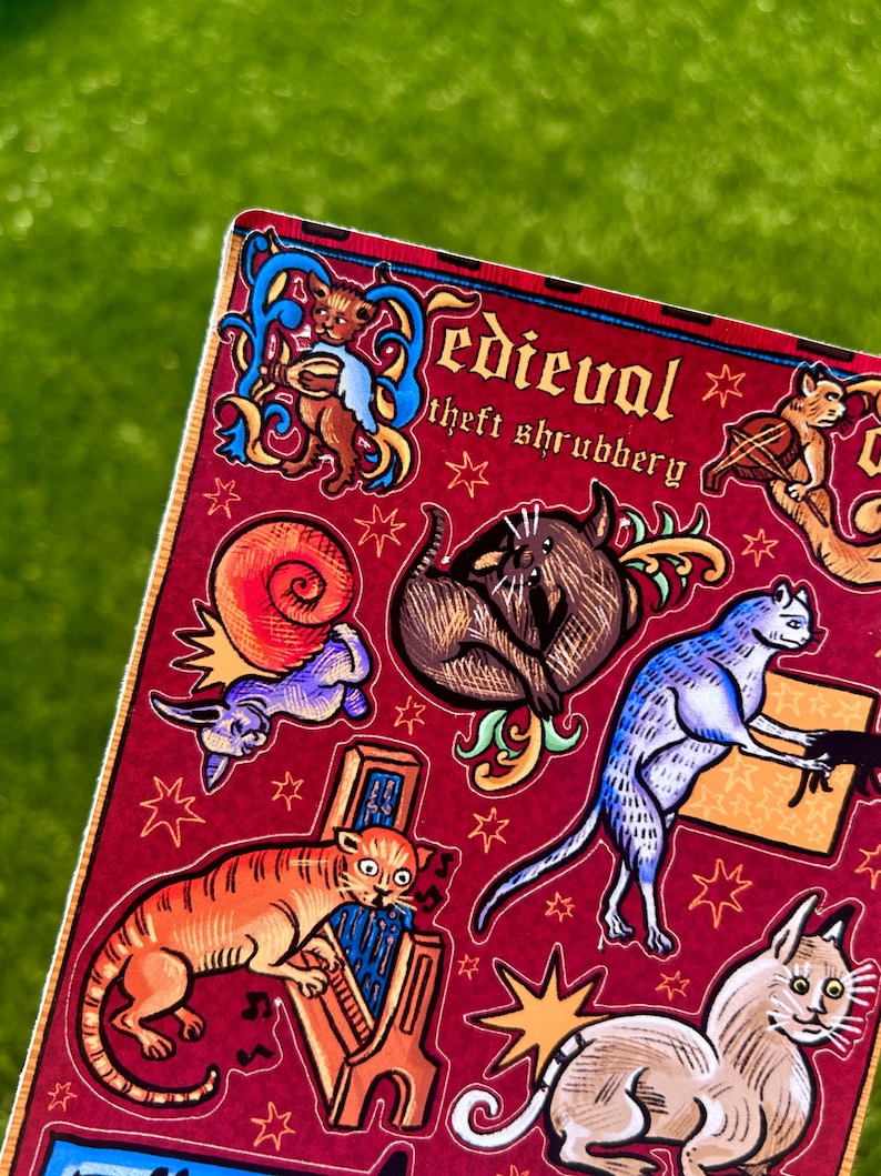 Puede incluir: Una hoja de pegatinas con un fondo burdeos que presenta ilustraciones de estilo medieval de gatos y otros animales. El texto "Medieval theft shrubbery" est&aacute; en la parte superior. Las ilustraciones son en tonos naranja, azul, marr&oacute;n y morado.