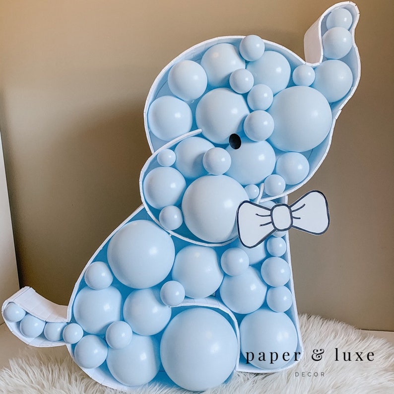 K&ouml;nnte beinhalten: Ein hellblaues Ballontier in Form eines Elefanten mit einer schwarzen Schleife. Der Elefant besteht aus vielen kleinen Ballons und steht auf einer wei&szlig;en Oberfl&auml;che. Der Text "paper & luxe decor" ist unten im Bild zu sehen.