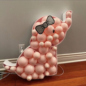 May include: A pink balloon animal shaped like an elephant with a black and silver bow. The elephant is made of many small balloons.