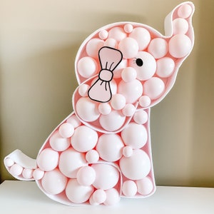 May include: A pink and white balloon animal shaped like an elephant with a black bow and eye. The elephant is made of many small balloons.