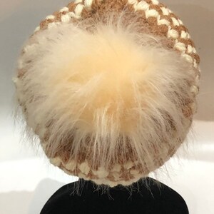 May include: A brown and white knitted beanie with a fluffy white pom pom on top.