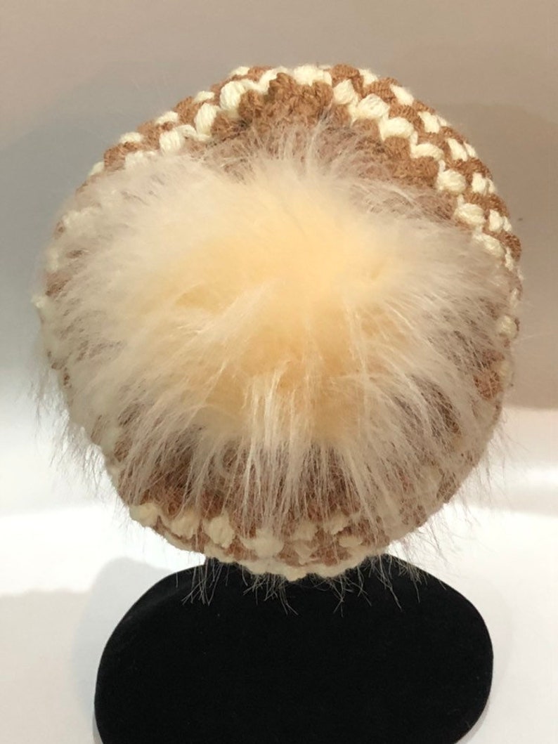 May include: A brown and white knitted beanie with a fluffy white pom pom on top.