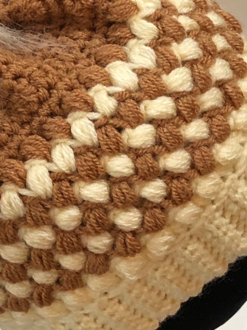 May include: Close-up of a brown and white crocheted hat with a textured pattern. The hat is made with two different shades of yarn, creating a striped effect.