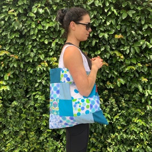 May include: A woman is holding a blue and white patchwork tote bag with a floral pattern. The bag has a red strap.