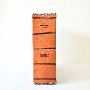 May include: An orange box file with black decorative lines and the text "THE MIDGET BOX FILE" and "FOR HOME AND COMMERCIAL USE". The box has a textured surface and a patterned border.