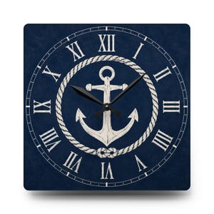 May include: A square wall clock with a dark navy blue background featuring a white anchor illustration encircled by a rope design. The clock face displays white Roman numerals from I to XII and includes two black clock hands at the center.