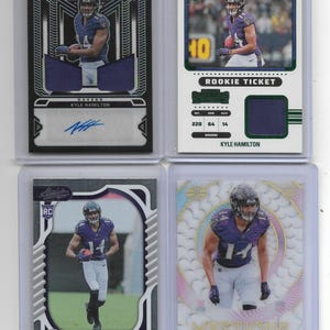 Peut inclure: Quatre cartes de collection de football américain rookie de Kyle Hamilton dans des étuis de protection en plastique. Les cartes présentent des photos d'action du joueur en uniforme violet des Ravens de Baltimore, dont une carte Obsidian autographiée.