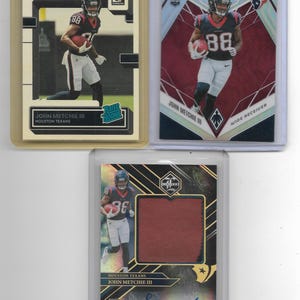 May include: Three sports trading cards featuring John Metchie III of the Houston Texans. One card is a Donruss Rated Rookie, one is a Panini Phoenix rookie card, and one is a Limited card with a fabric swatch and a blue ink autograph signature.