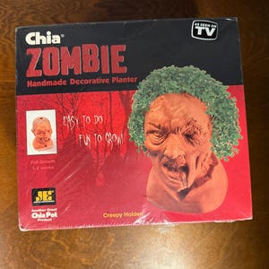 May include: A red and black box with the words "Chia Zombie Handmade Decorative Planter" on the front. The box features a picture of a zombie-like planter with green hair. The text "Easy to do Fun to Grow!" is also on the box.