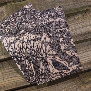 May include: Two cream-coloured notebooks with black ink illustrations of a tree and a bird. The tree has intricate branches and the bird is perched on a branch.