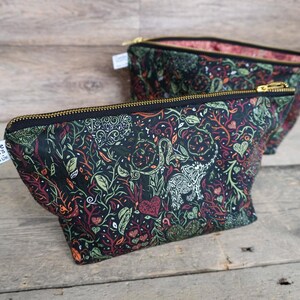 May include: Two black fabric pouches with a colorful botanical pattern featuring leaves, vines, and hearts. The pouches have gold zippers and are labeled "Cuttle Prints". The interior lining is a pink floral pattern.