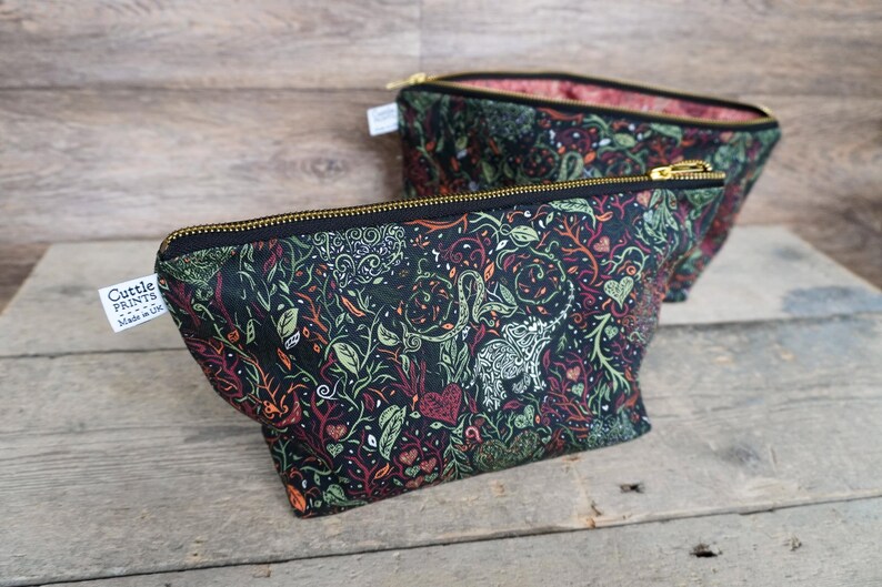 May include: Two black fabric pouches with a colorful botanical pattern featuring leaves, vines, and hearts. The pouches have gold zippers and are labeled "Cuttle Prints". The interior lining is a pink floral pattern.