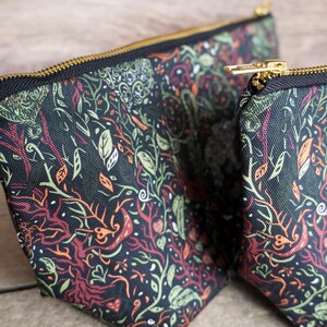 May include: Two zippered pouches with a dark background and a colorful botanical pattern. The design includes green, orange, and red plant elements. The pouches have gold-colored zippers and a white tag that reads "Cuttle Prints - Made in UK."