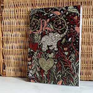 May include: A black notebook with a colorful design featuring an elephant, hearts, and floral patterns. The cover is made of a textured paper.