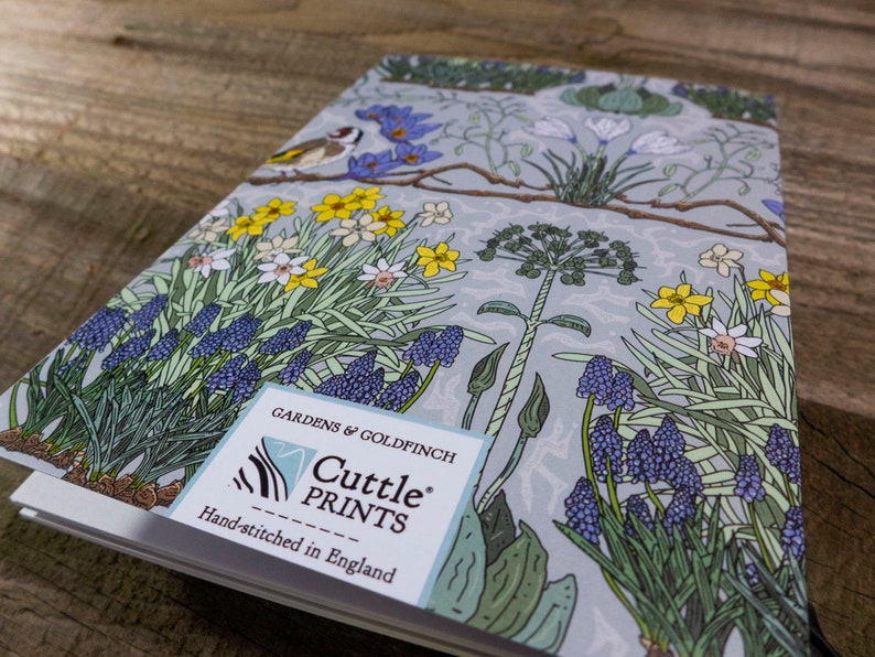 May include: A blue and green floral notebook with a goldfinch and the text "Gardens & Goldfinch Cuttle Prints Hand-stitched in England" on the front cover.