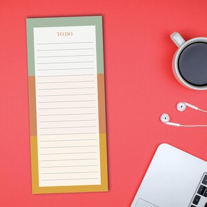 May include: A colorful to-do list notepad with the word "TO DO" at the top. The notepad has a green, brown, and yellow color block design. A white coffee mug, white earbuds, and a laptop are on a red background.