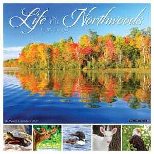May include: A 2027 18-month wall calendar titled Life in the Northwoods by M. Crowley. The cover features a vibrant autumn forest reflecting on a blue lake. Five smaller images show a turtle, a deer, a loon, a white deer, and a bald eagle.