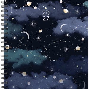 May include: A spiral-bound planner featuring a dark navy blue night sky cover with white clouds, glowing stars, crescent moons, and various planets with rings. The text 20 27 is printed in white in the center of the cover, surrounded by celestial patterns.