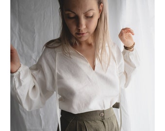 Blusa in morbido lino naturale con maniche a sbuffo. Blusa con scollo a V in stile boho. Top in lino a maniche lunghe con allacciatura al collo. Blusa in lino dalla vestibilità ampia.