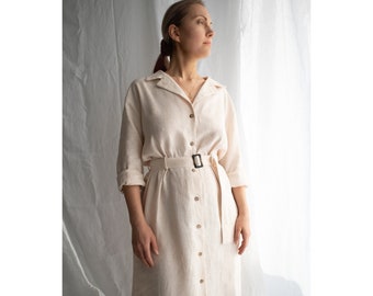 May include: A long-sleeved, cream-colored linen dress with a button-down front and a black belt. The dress has a relaxed fit and a midi length.