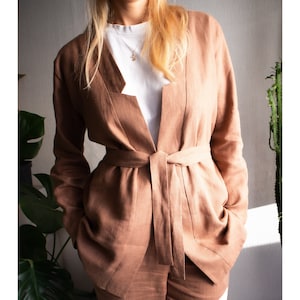 Könnte beinhalten: Eine braune Leinenjacke mit langen Ärmeln und einem passenden Gürtel. Die Jacke hat einen tiefen V-Ausschnitt und eine lockere Passform.